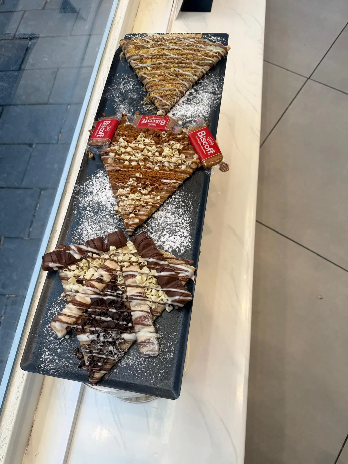 Folded crêpes on a slate board with Lotus biscuit and icing sugar