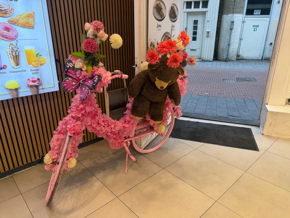 A pink bicycle covered in flowers beside the shop door, looking out onto the Nieuwendijk