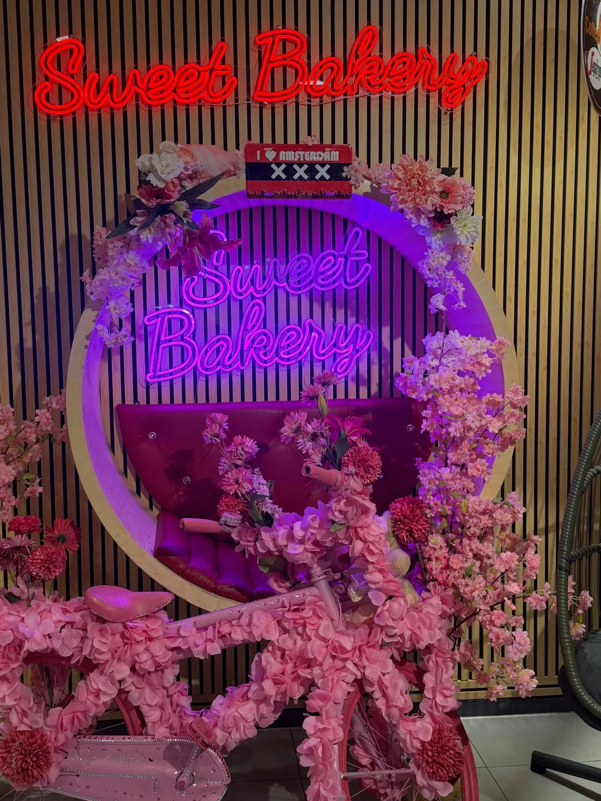 The Sweet Bakery neon sign on a wall of pink blossom inside the shop