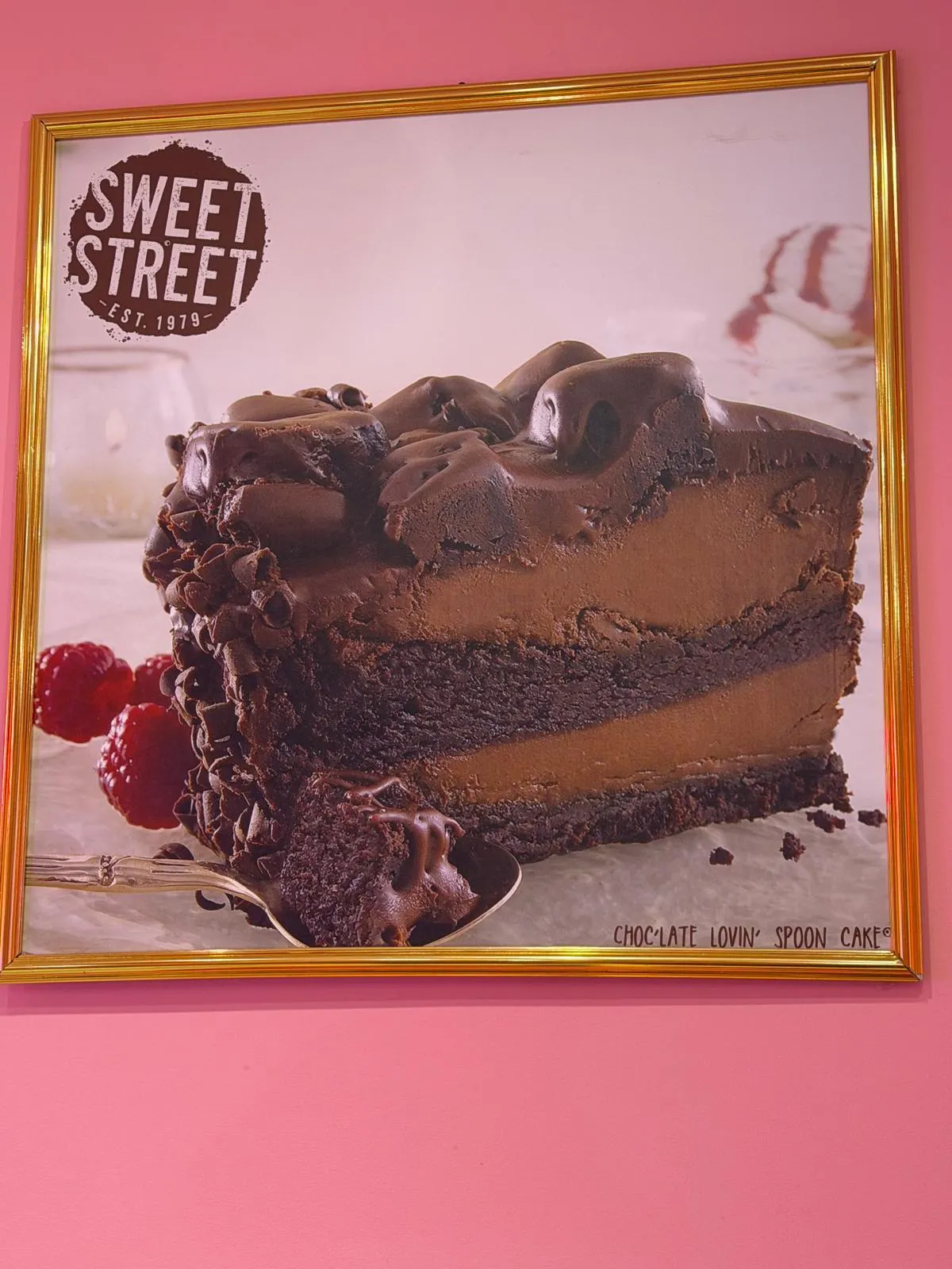 A framed Sweet Street print of a chocolate layer cake on the pink wall in the shop